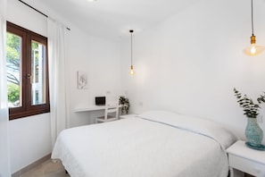 Ein Schlafzimmer mit Bett, Schreibtisch, Stuhl, Pendelleuchte und einem Fenster mit Vorhängen.