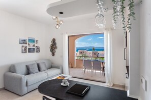 Ein modernes Wohnzimmer mit einem grauen Sofa, einem schwarzen Tisch mit einem Tablet und einer Tasse sowie einem Balkon mit Meerblick.