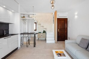 Eine moderne Küche mit weißen Schränken, ein Essbereich mit Tisch und Stühlen, eine Treppe zu einem Wohnbereich mit einer Couch und einer Zeitschrift auf einem Couchtisch.