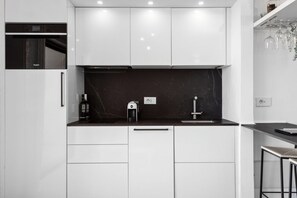 Eine moderne Küche mit weißen Schränken, einer schwarzen Arbeitsplatte, einer Kaffeemaschine und einem Weinregal.