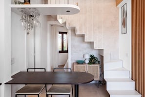A modern dining area with a dark wooden table, white walls, and a staircase leading to an upper level.