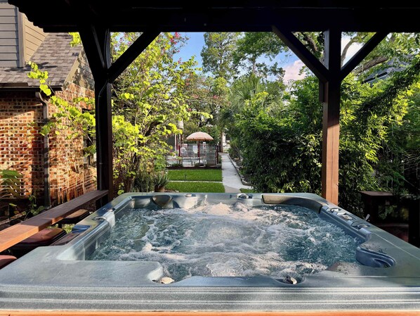 A hot tub with a wooden deck, surrounded by a brick wall and lush greenery.