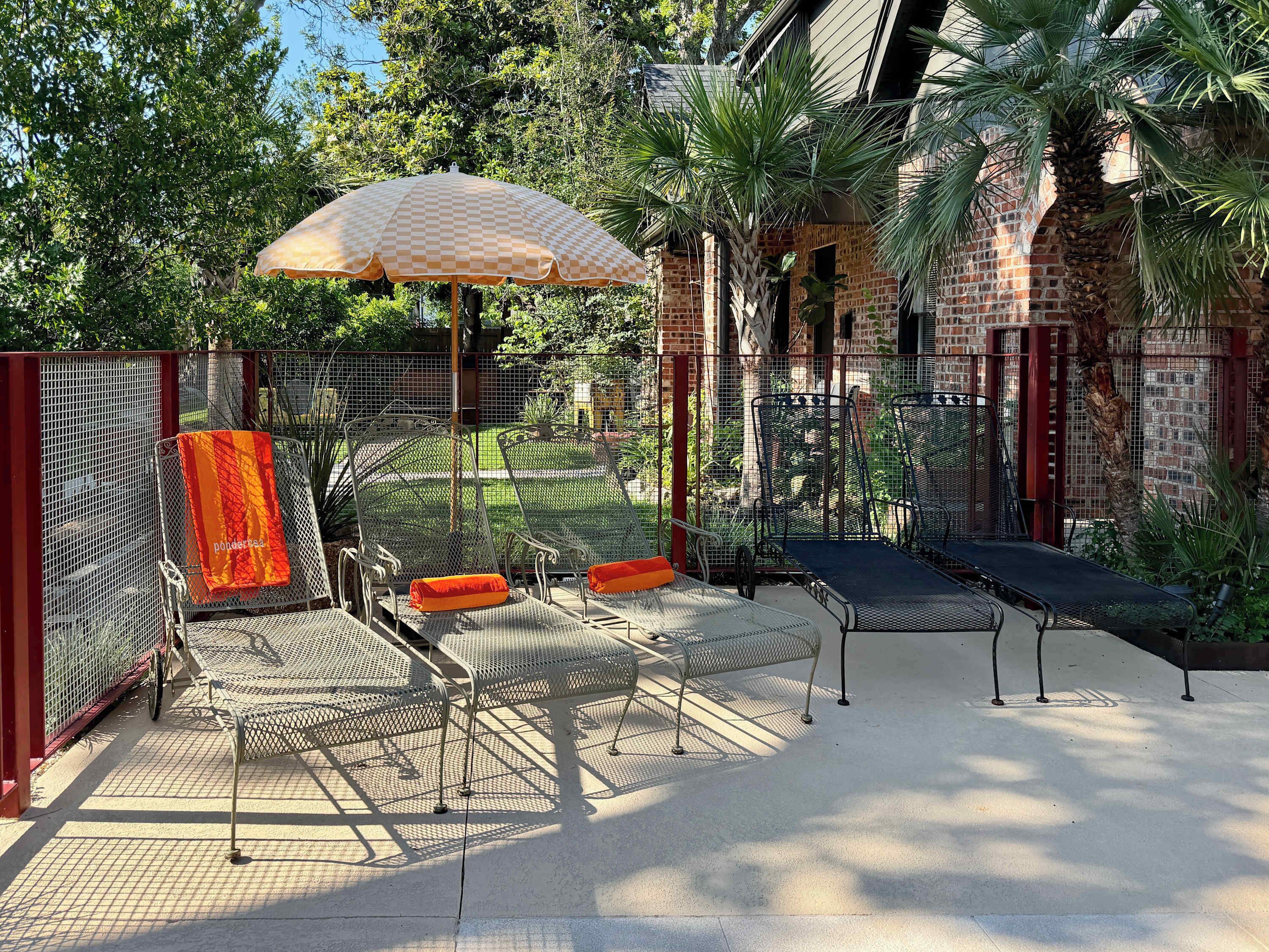 A patio with metal chairs and a table, a checkered umbrella, and a brick wall.