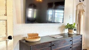 A room with a dark wooden dresser, a flat-screen TV mounted on the wall, a door with a light switch, and a potted plant on the dresser.