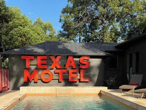 A motel sign with a pool area and lounge chairs.
