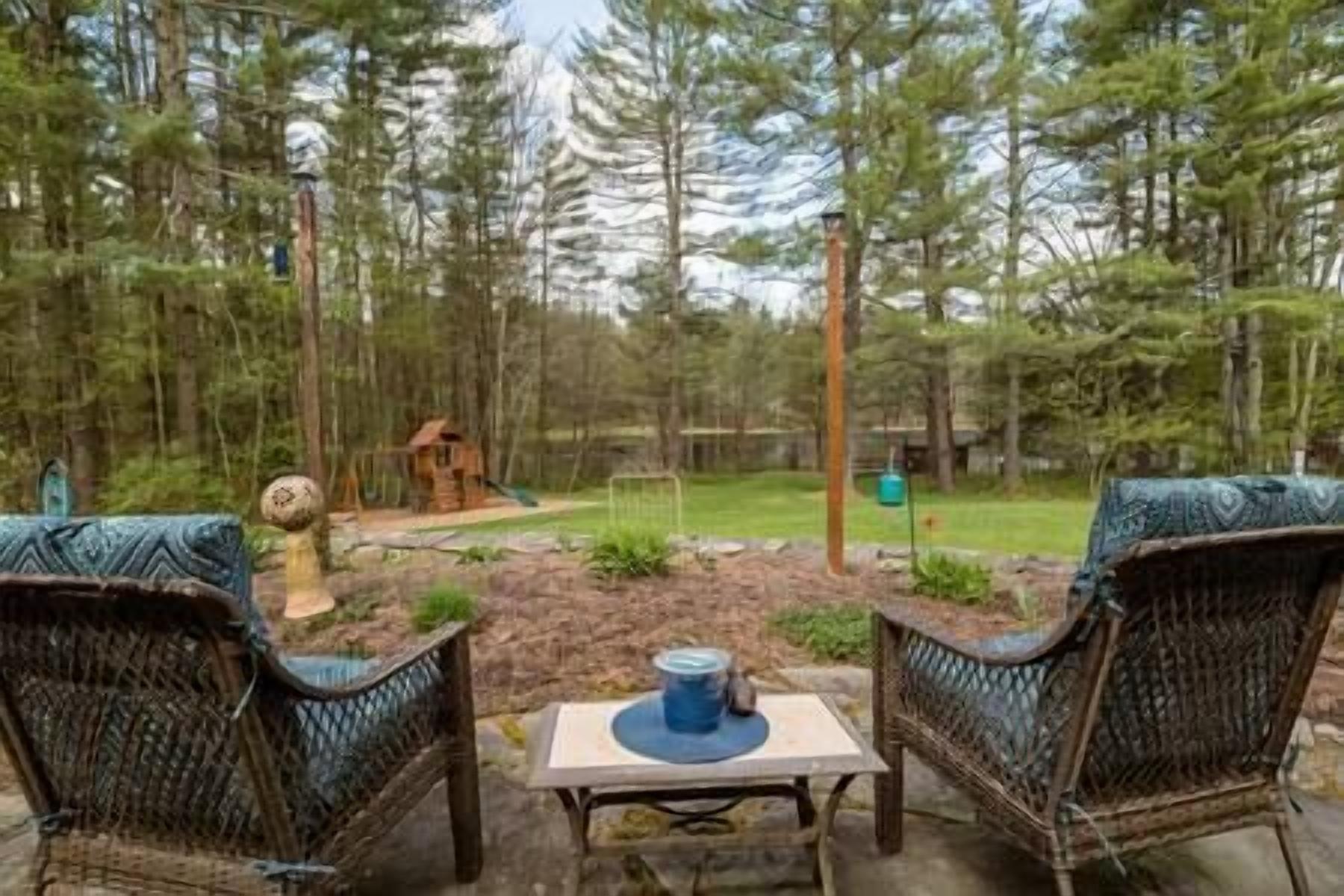 An outdoor seating area with wicker chairs and a table, surrounded by a forested landscape.