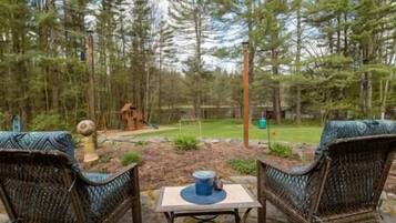 An outdoor seating area with wicker chairs and a table, surrounded by a forested landscape.