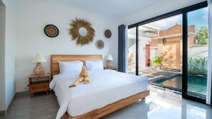A modern bedroom with a large bed, wooden headboard, and a glass door leading to a pool area. - Casa de Cavendish (Canggu)