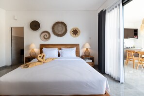 A hotel room with a large bed, two bedside lamps, a wooden headboard, and wall decor. - Casa de Cavendish (Canggu)