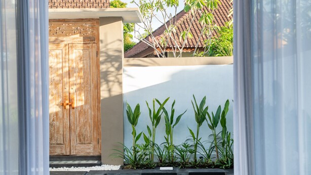 A pool area with a wooden door, a white wall, and green plants. - Casa de Cavendish (Canggu)