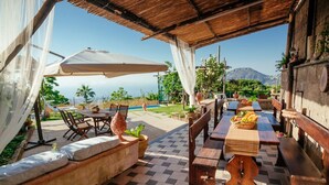 An outdoor patio with a checkered floor, wooden tables and benches, and a view of the ocean.