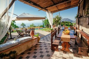 Un patio al aire libre con piso a cuadros, mesas y bancos de madera, y vista al océano.
