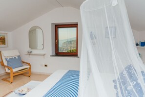 Un dormitori amb un llit, una cadira, una finestra amb vistes i un mirall.