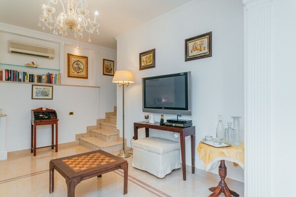 A living room with a chandelier, a television, a bookshelf, a chess table, and a staircase.