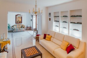A spacious living room with a beige sofa, a chess table, and a chandelier.