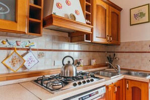 A kitchen with wooden cabinets, a gas stove, and a stainless steel kettle.