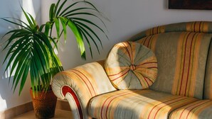 Un canapé doté d’un revêtement à rayures et d’un dossier capitonné, placé à côté d’une plante en pot aux longues feuilles vertes.