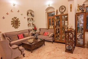 A living room with a sofa, armchair, and coffee table, featuring decorative items and a cabinet with glass doors. - Amã Stays & Trails Butterfly Villa, Deolali, Nashik (Nashik)