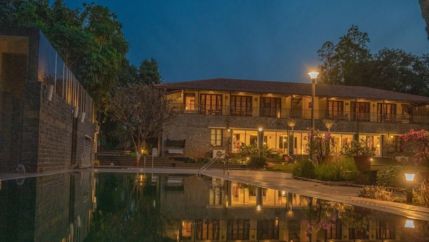 A two-story building with a pool in front, surrounded by trees and potted plants. - Amã Stays & Trails Butterfly Villa, Deolali, Nashik (Nashik)