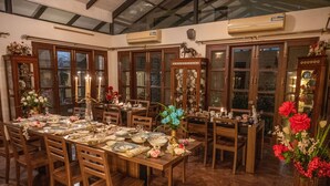 A dining area with wooden tables and chairs, glass cabinets, and floral centerpieces. - Amã Stays & Trails Butterfly Villa, Deolali, Nashik (Nashik)