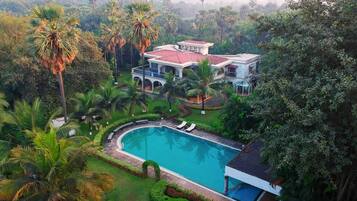A large house with a swimming pool surrounded by lush greenery and palm trees.