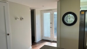 Um corredor com porta dando para um quarto, um relógio na parede e uma porta com painéis de vidro fosco.