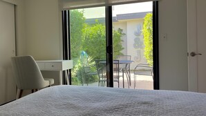 Quarto de hotel com cama, escrivaninha e vista para o pátio externo.