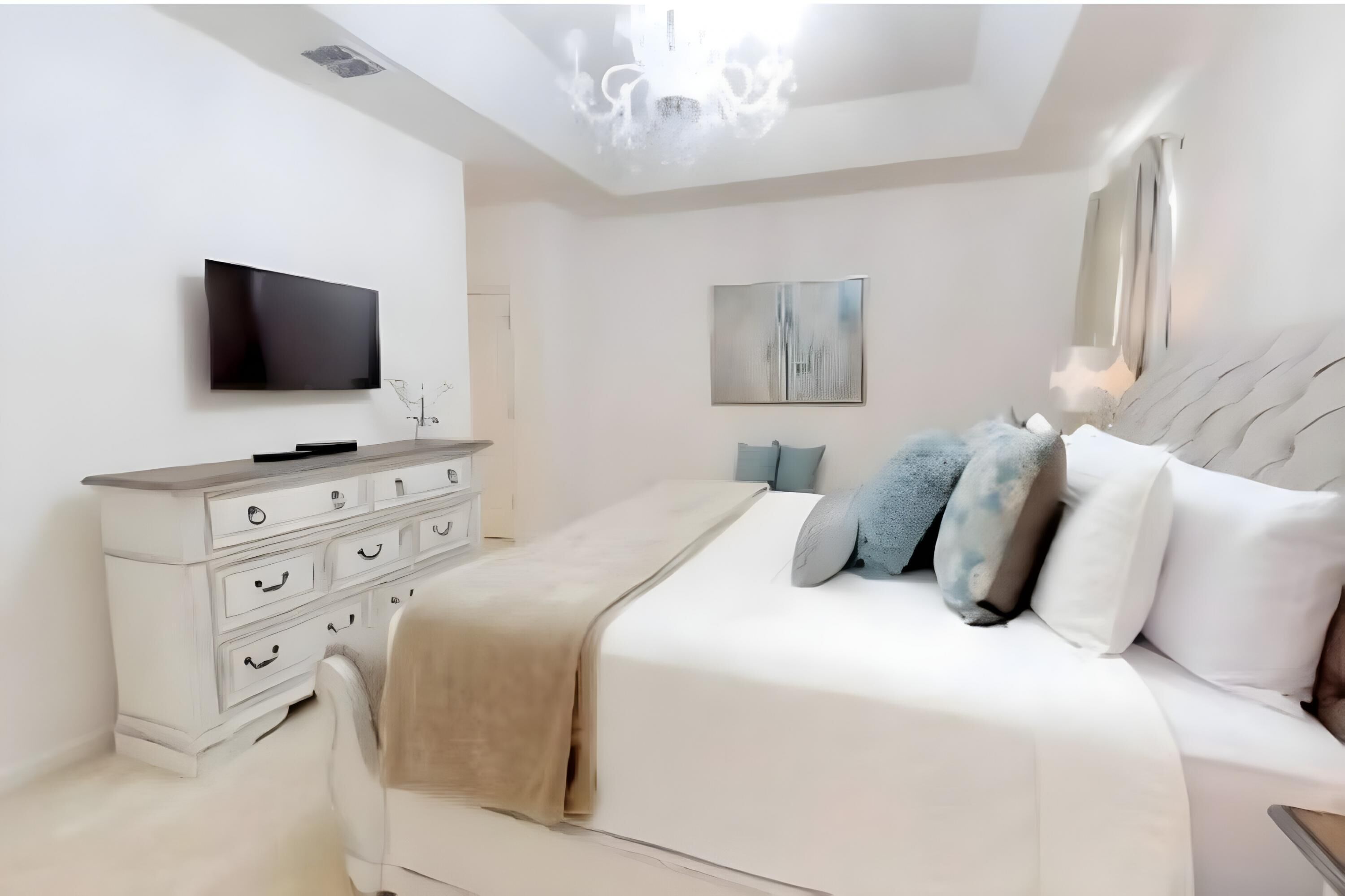A modern bedroom with a large bed, a TV mounted on the wall, a dresser, and a painting on the wall.