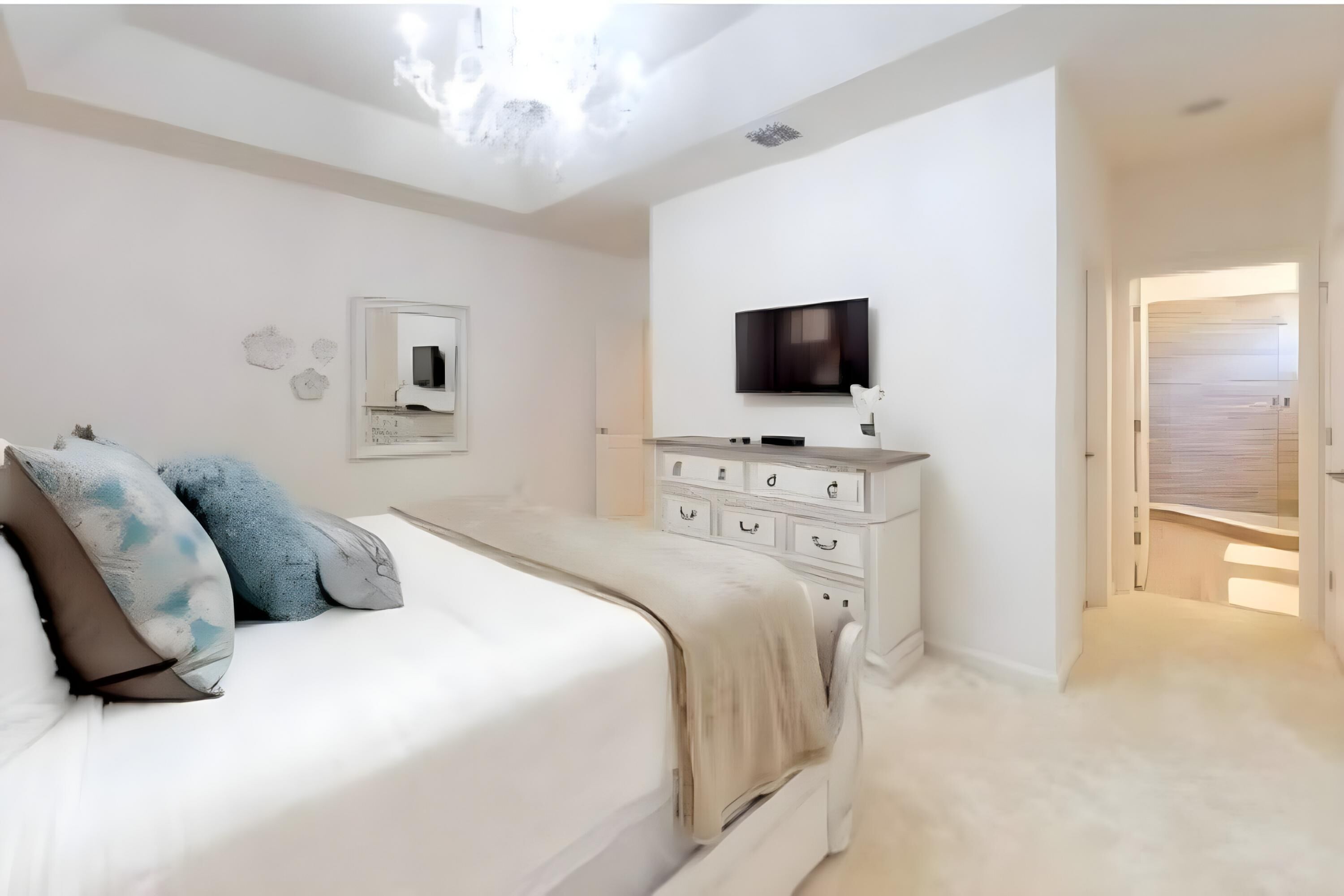 A bedroom with a bed, a dresser, a TV, and a door leading to another room.
