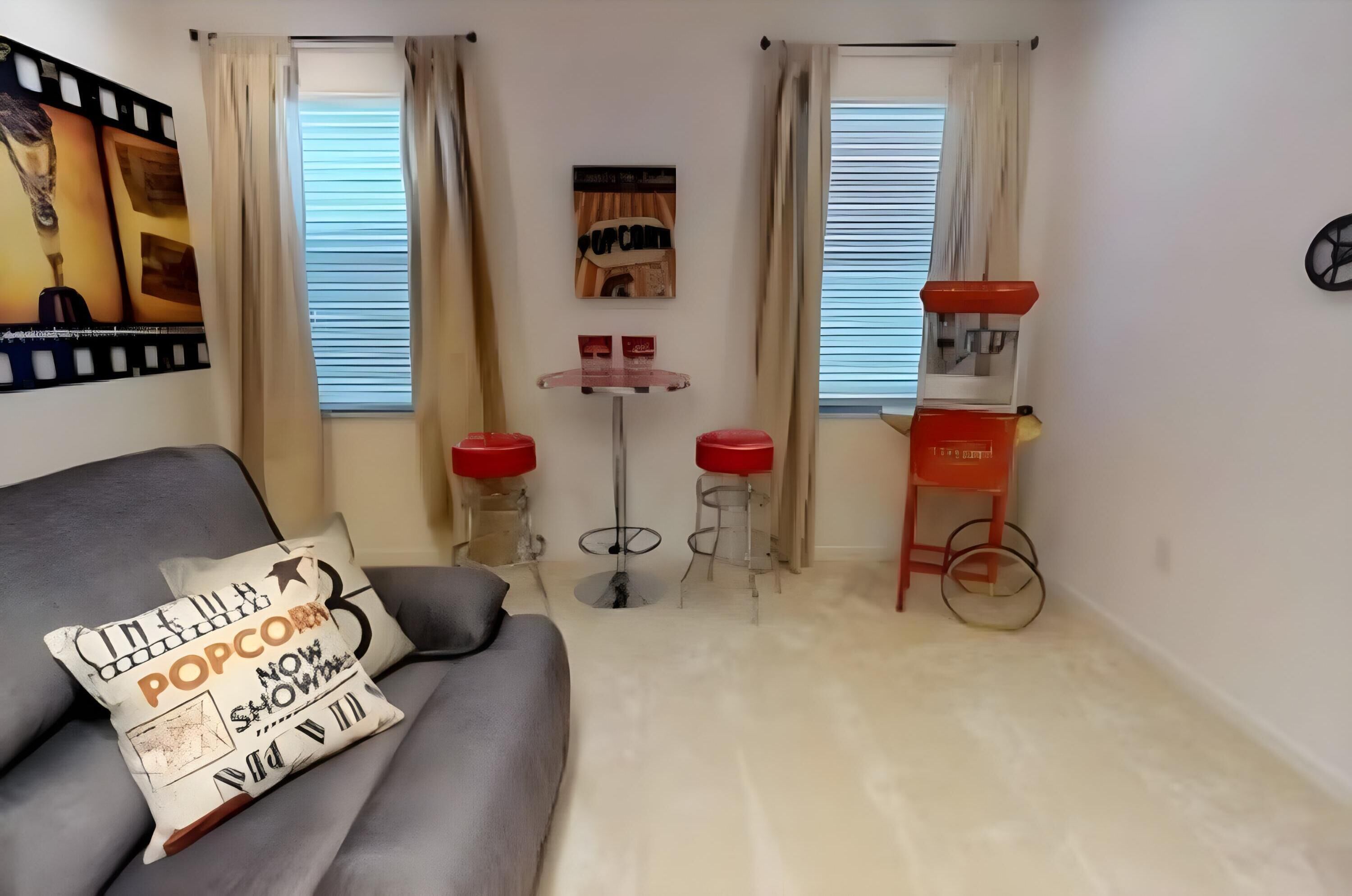 A living room with a grey sofa, a small table with two red stools, and a red and white speaker.