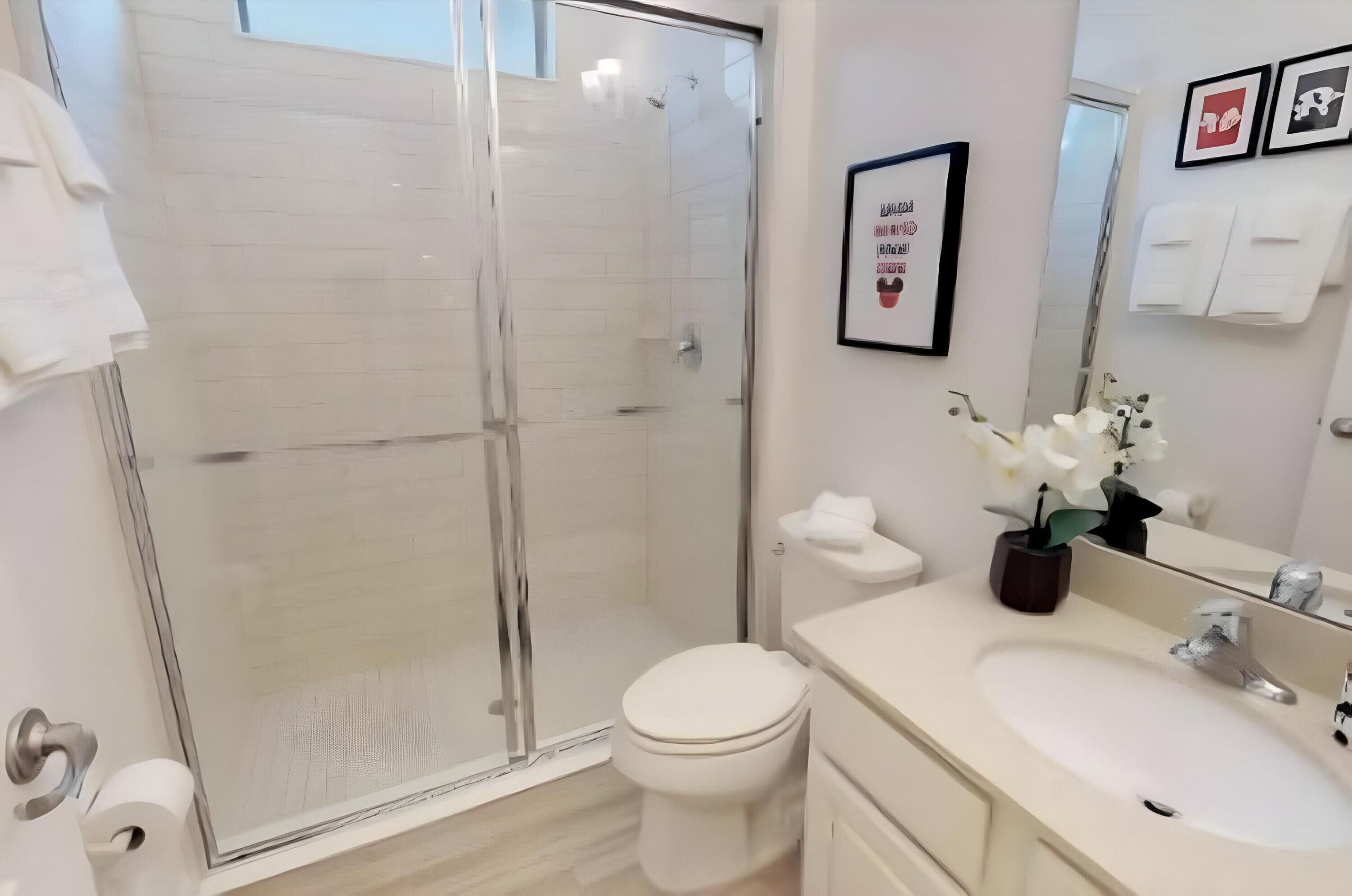 Et moderne badeværelse med brusekabine i glas, toilet, vask med spejl og et indrammet inspirerende citat på væggen.