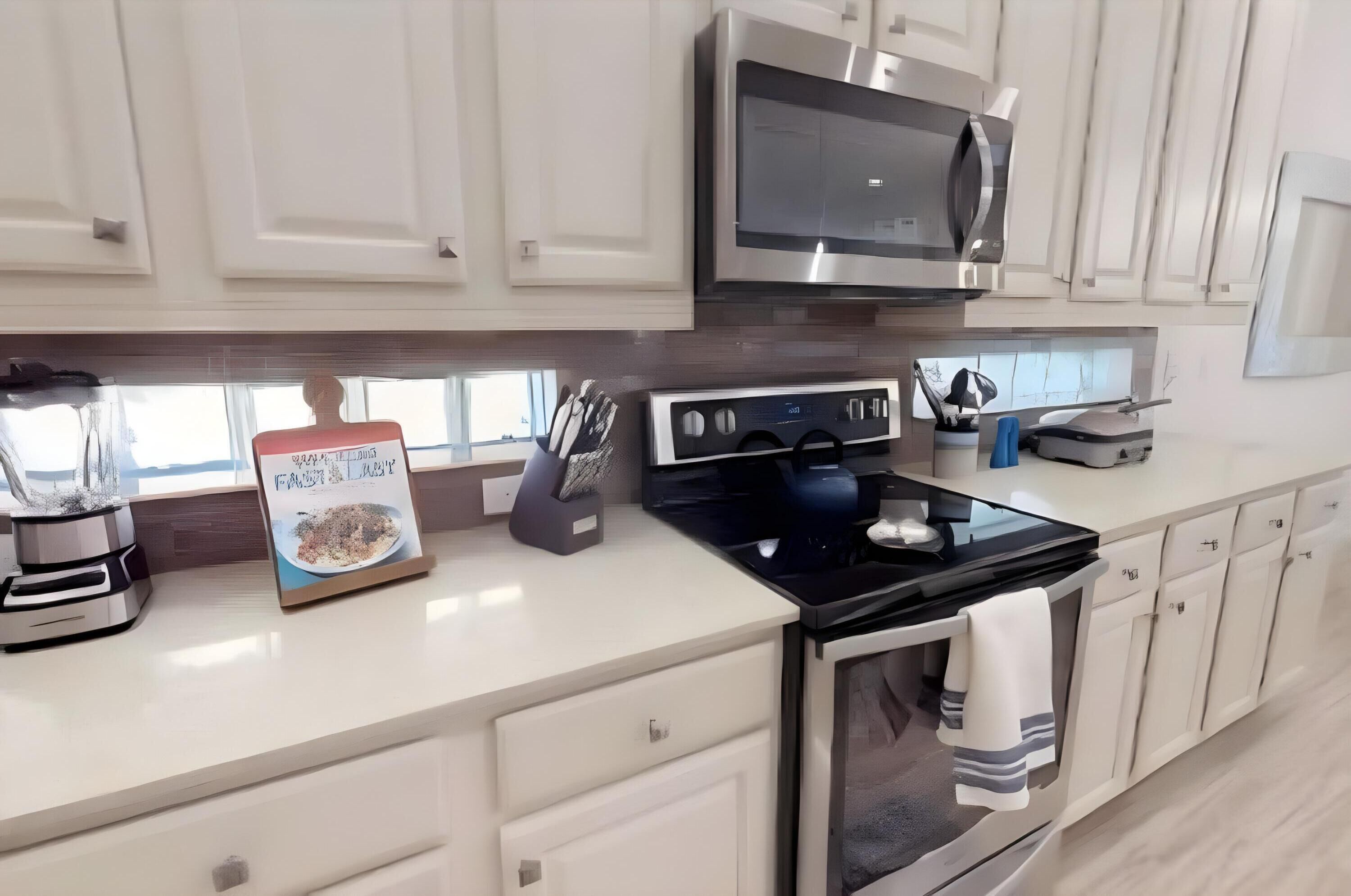 A modern kitchen with white cabinets, a stainless steel microwave, a black stove, and a coffee maker.