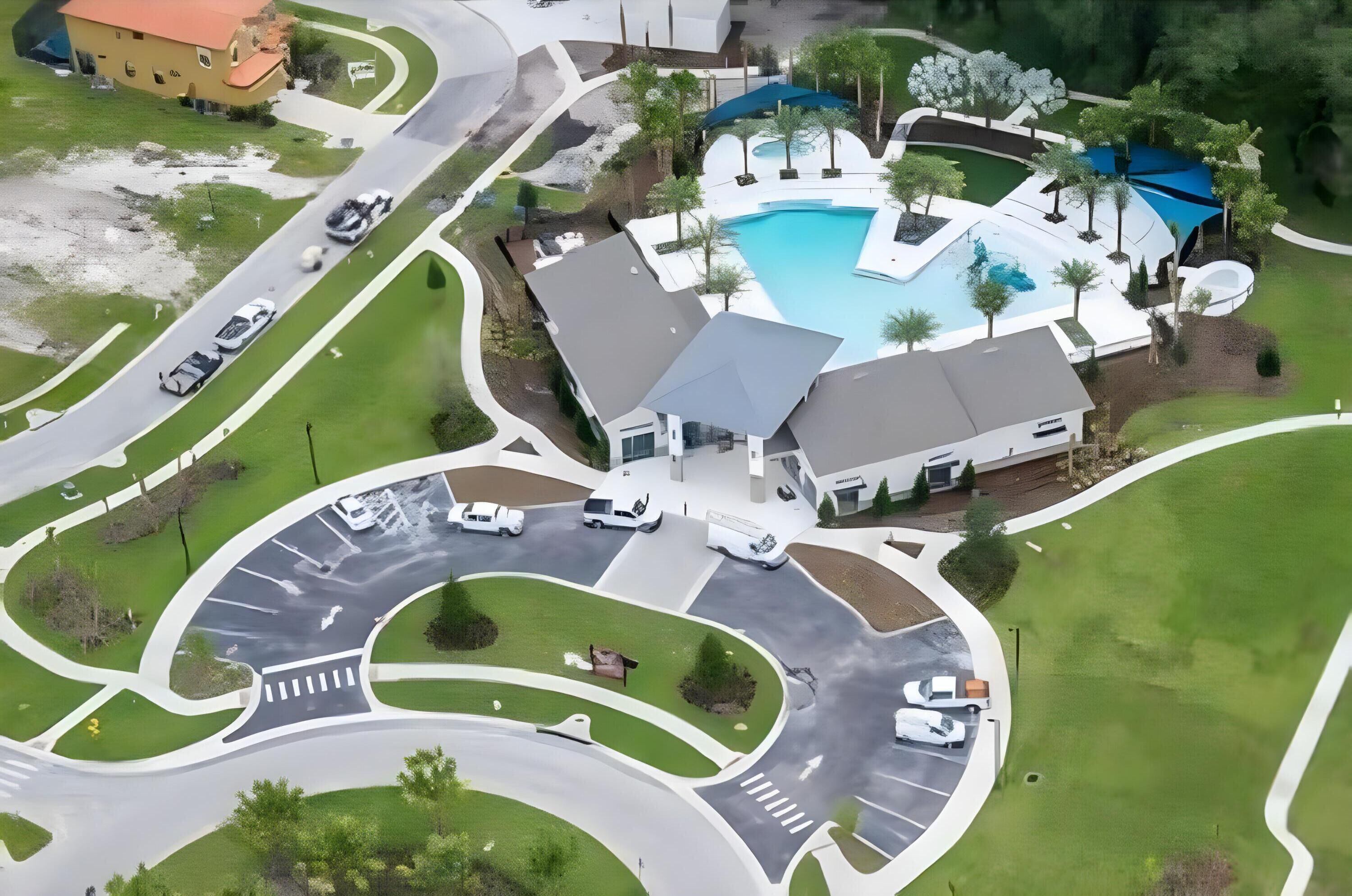 An aerial view of a modern complex with a swimming pool, landscaped areas, and a parking lot.