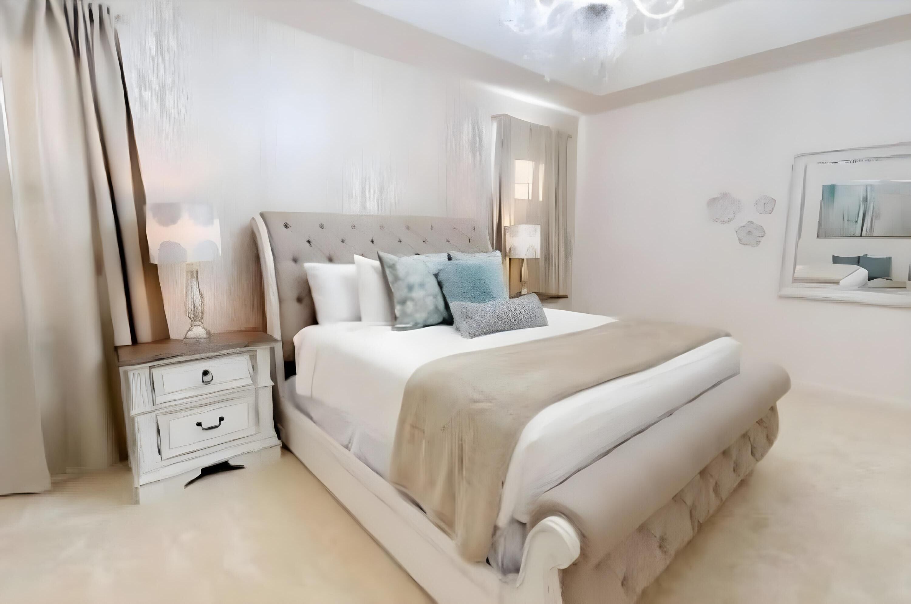 A bedroom with a large bed, bedside tables, a nightstand, a mirror, and a wall-mounted light fixture.