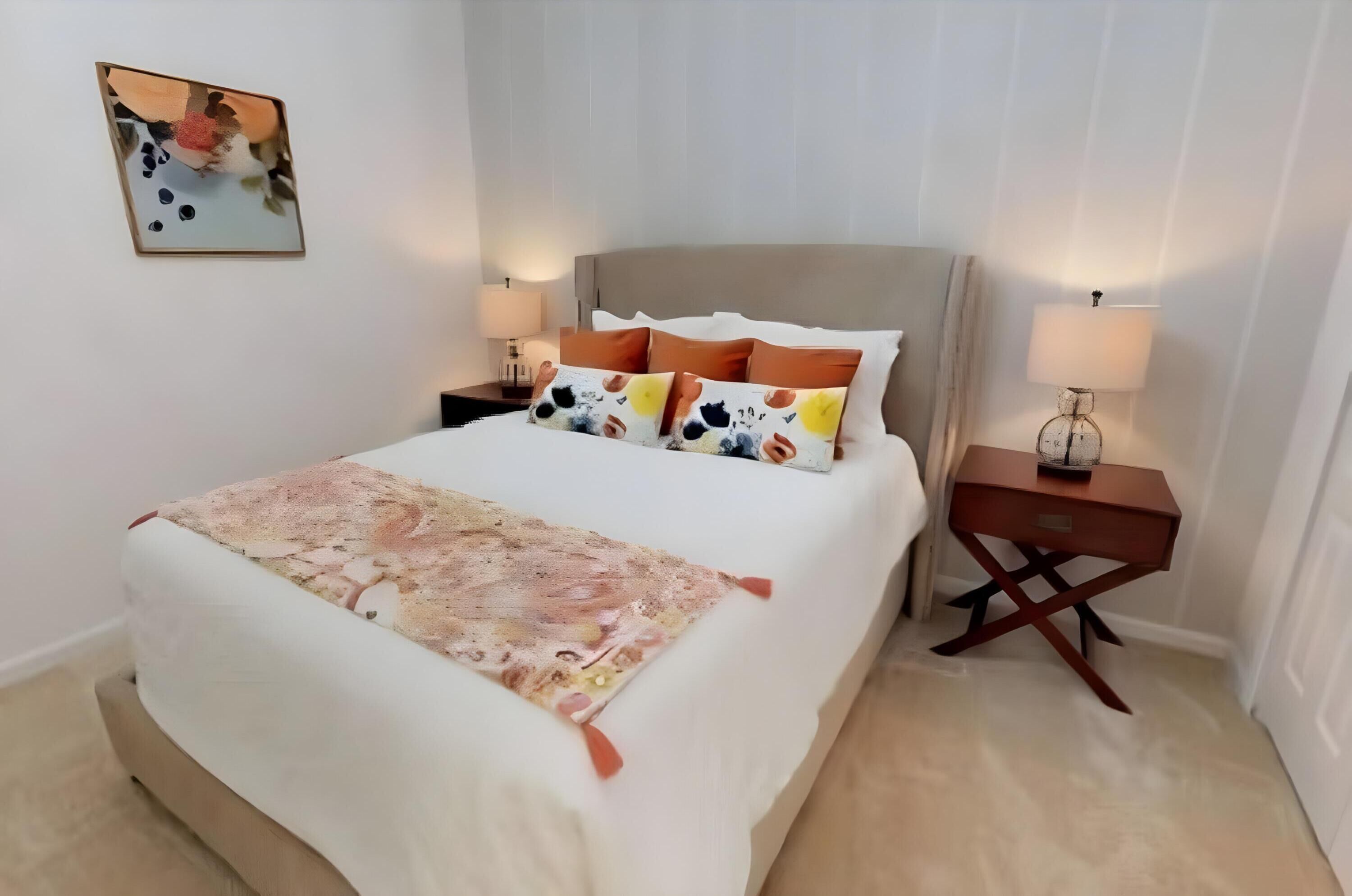 A neatly made bed with a patterned blanket, a headboard, and multiple pillows. There is a bedside table with a lamp and a decorative item.