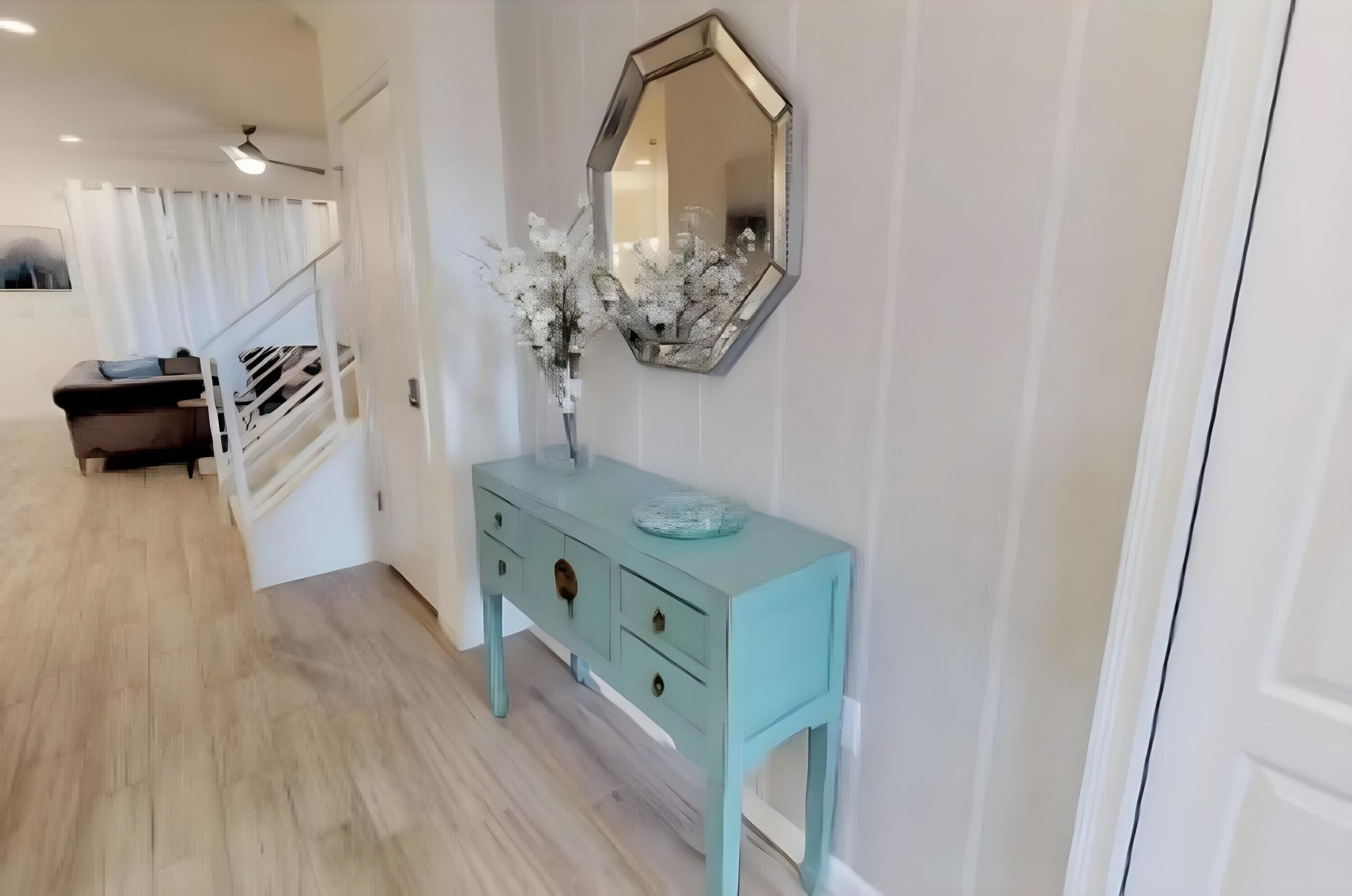 A hallway with a light blue console table, a mirror, and a vase with white flowers.