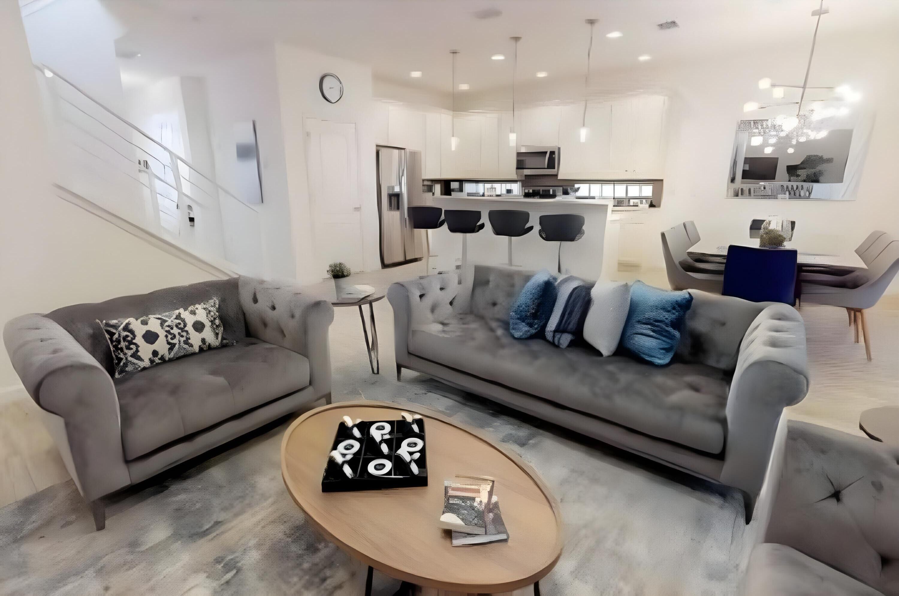 A modern living room with two grey sofas, a coffee table, and a dining area with a table and chairs.