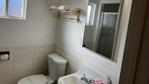 Casa de banho com sanita, lavatório e espelho. Tem uma janela e um porta-toalhas.