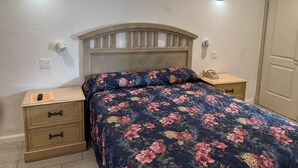 Um quarto com colcha floral, cabeceira de madeira, mesas de cabeceira com abajures e uma porta.