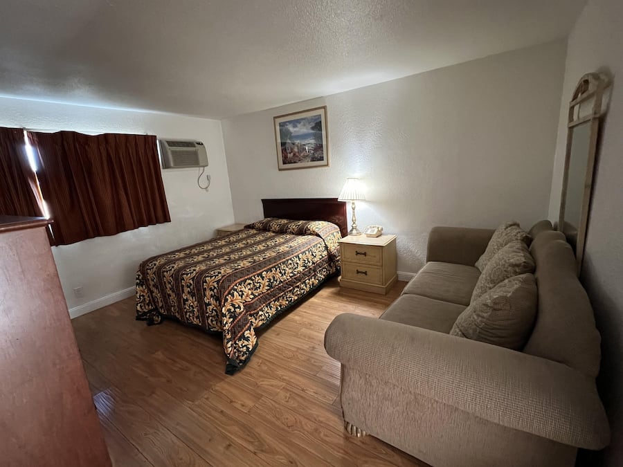 Un dormitorio con cama, mesita de noche, lámpara, sofá y un cuadro en la pared.