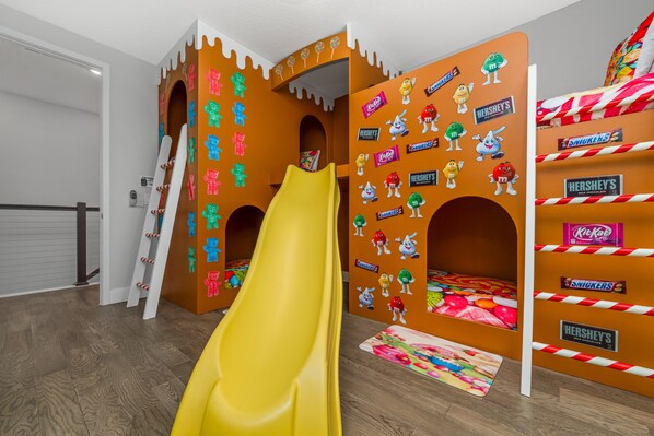 A children's play area with a yellow slide, decorated with candy-themed wall stickers and a candy-striped bed.