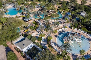 An aerial view of a resort with multiple swimming pools, palm trees, and lounge areas.