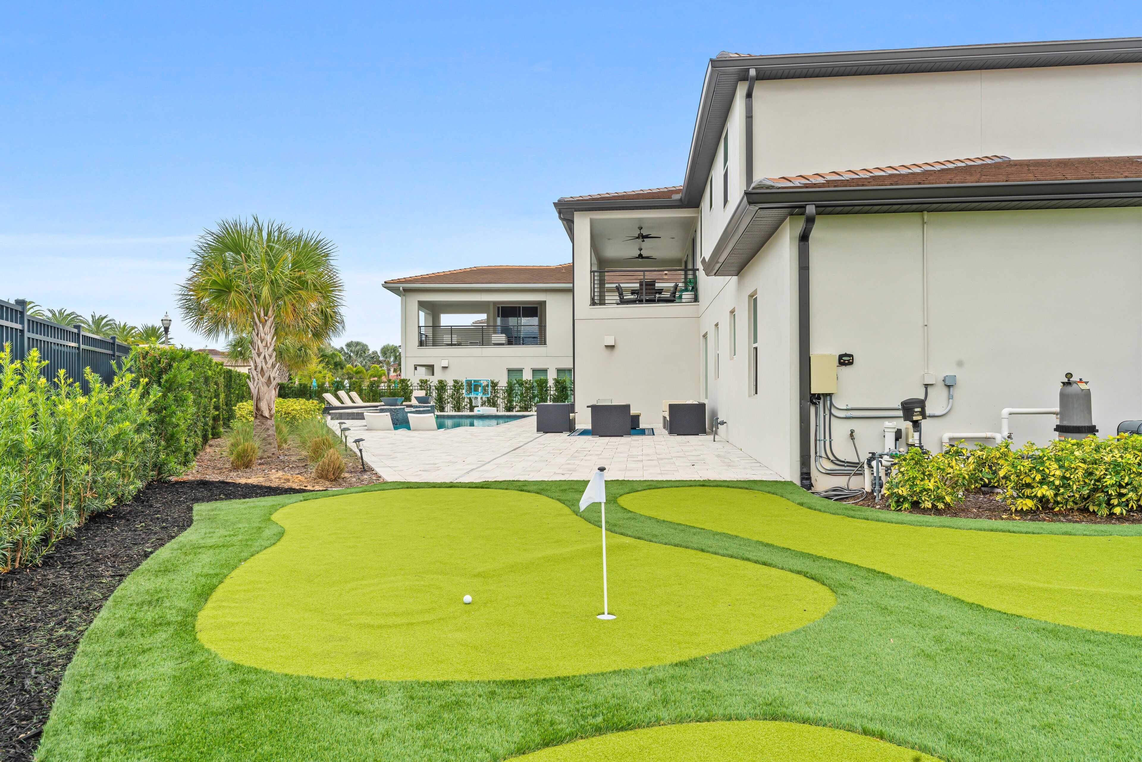 A golf course with a putting green, a pool, and a building with a balcony.
