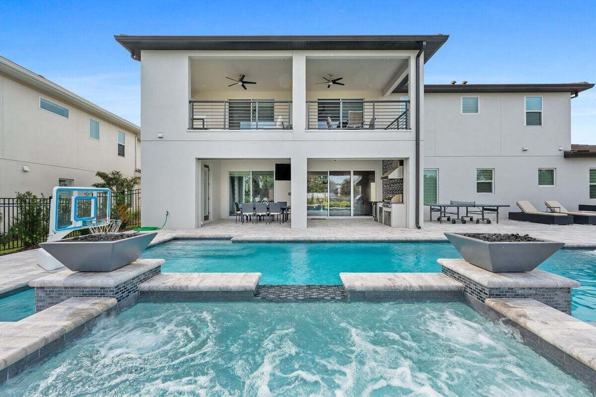 A two-story modern house with a swimming pool in the foreground.