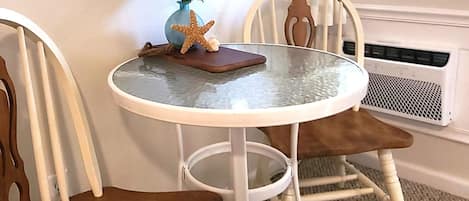 A round table with a glass top, surrounded by two wooden chairs with curved backs. A small plant with green leaves and a starfish decoration are on the table.