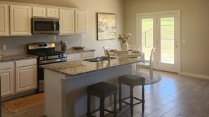 A spacious kitchen with a central island, white cabinetry, stainless steel appliances, and a large window providing natural light. - Entire New home in Edmond, Oklahoma (Edmond)