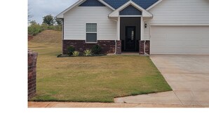 A single-story house with a garage, a front door, and a small front yard with grass and plants. - Entire New home in Edmond, Oklahoma (Edmond)