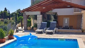 Une piscine avec un flotteur en forme de requin, des chaises longues et un espace patio couvert.