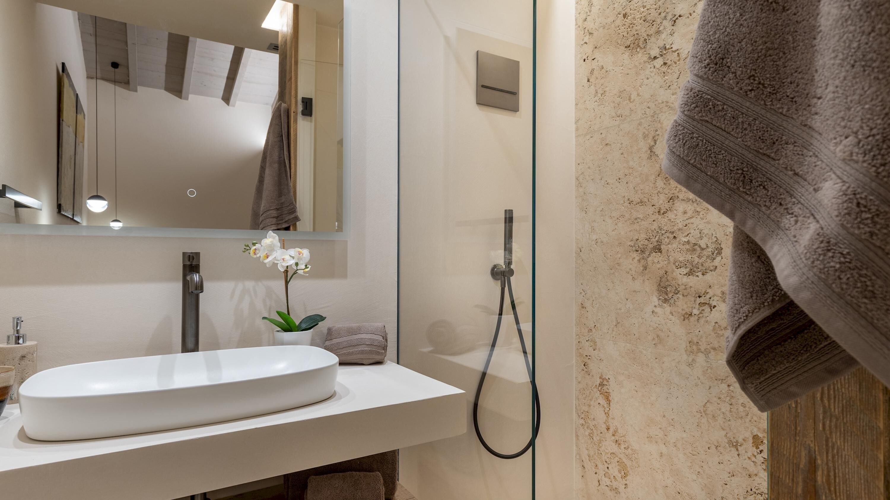 Ein modernes Badezimmer mit einem weißen Waschbecken, einer Duschkabine aus Glas und einem Handtuch an der Wand.
