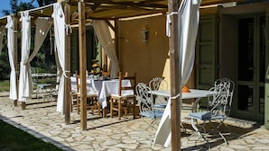 Une terrasse extérieure avec des tables et des chaises, abritée par une pergola agrémentée de rideaux blancs.